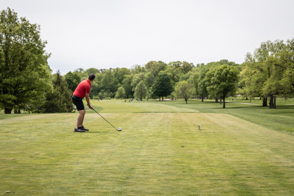 Guy in red shirt on a golf course about to tee off.